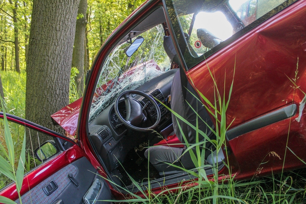 Verunfalltes rotes Auto vor einem Baum
